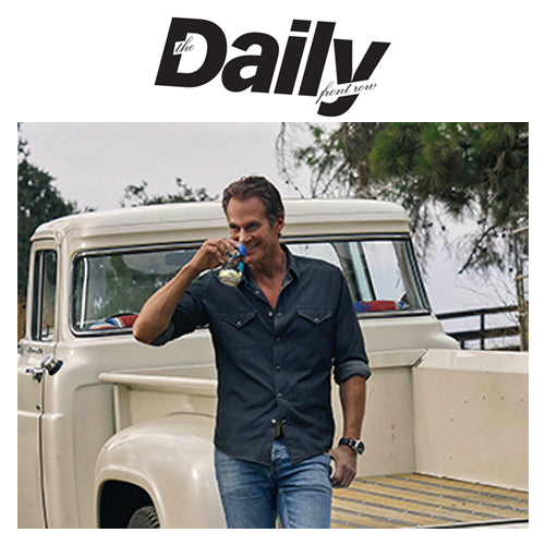 Man sipping a drink while leaning on the tailgate of a cream vintage pickup truck outdoors, headline ‘The Daily front row’ above