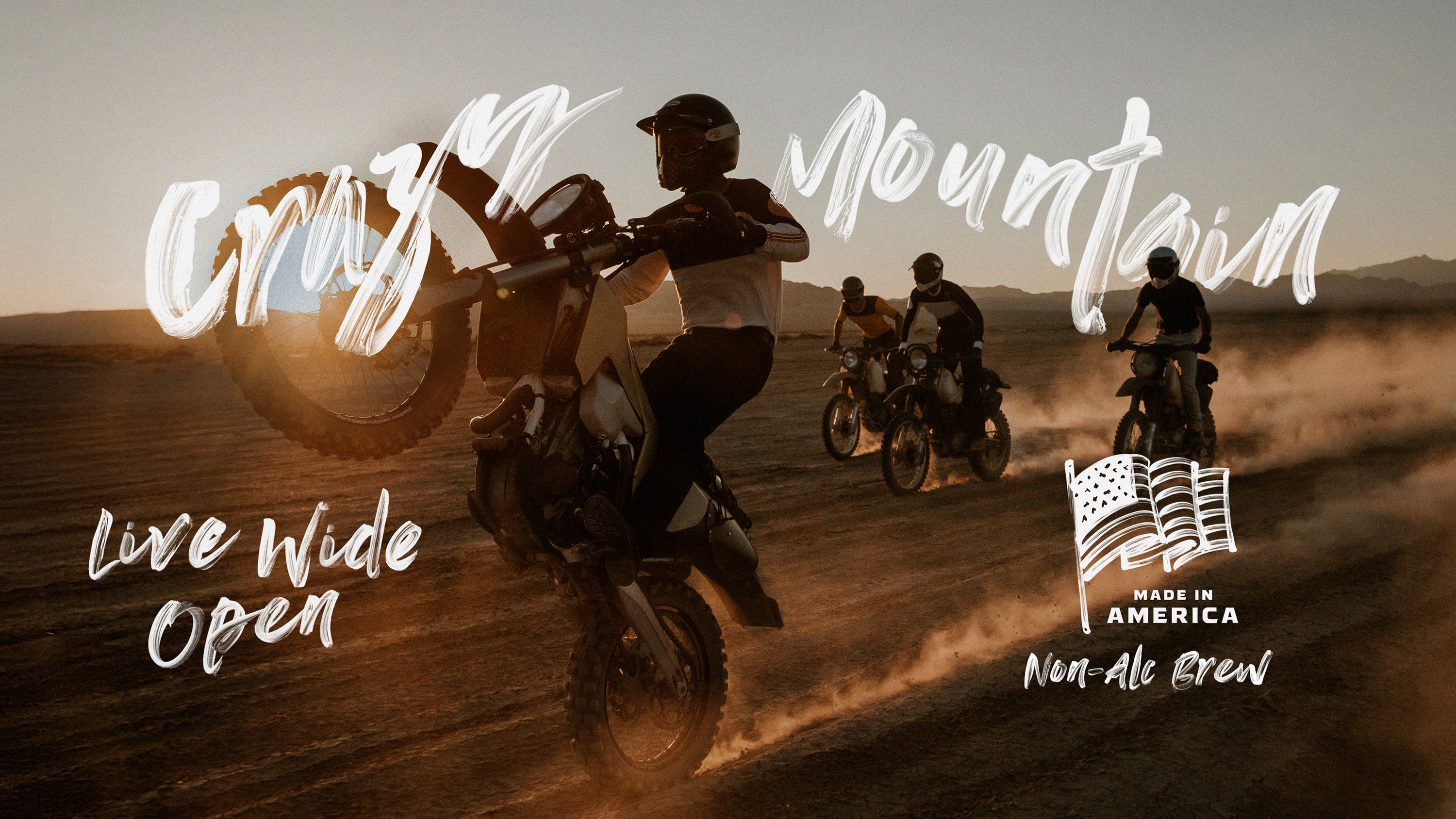Motorcyclists riding on a dirt road with 'Crazy Mountain' branding and text, reading 'Live Wide Open' and 'Made in America' 'Non-Alc Brew'.